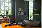 Frei stehende Beton-Badewanne im Badezimmer mit grauen Wänden und Industriefenster, gerahmte Schallplattenhüllen als Wanddekoration