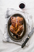 Roasted chicken on metallic tray with a knife and a glass of wine