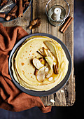 Sweet crepes with caramelized pears, cinnamon and almonds on wooden table