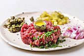 Beef tartare with quail egg in shell, cutting pickled cucumbers, capers, red onion, chives and arugula salad