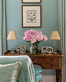 Pink peonies on antique dressing table with framed photos and small lamps