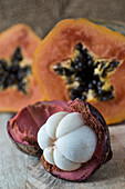 An opened mangosteen with a papaya in the background