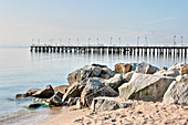 View across pile of boulders on beach to pier stretching out into sea