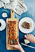 Hands slicing chocolate chip banana bread on a wooden cutting board