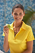A young brunette woman wearing a yellow polo shirt and holding an apple