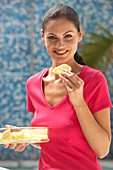 A young brunette woman wearing a pink top and holding a slice of pineapple