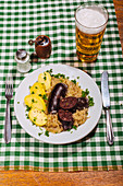 Black pudding with boiled potatoes and sauerkraut on a checked tablecloth, with pale beer