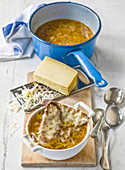 French onion soup in bowl and saucepan with baguette croutons and grated gruyere cheese