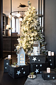Weiß geschmückter Weihnachtsbaum mit Windlichtern und Laternen auf grauen Holzkisten
