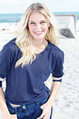 A young blonde woman on a beach wearing a long-sleeved blue shirt