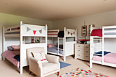 White wooden bunkbeds in childrens bedroom with armchair and decorative bunting