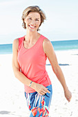 A mature woman on a beach wearing a salmon-coloured top and colourful trousers