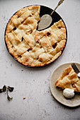 Apple pie with lattice decoration and a slice served on handmade ceramic plate with a scoop of vanilla ice-cream