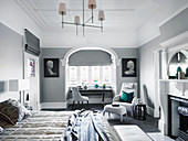 Elegant bedroom with fireplace, armchair with footstool and table in front of bay window