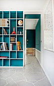 Turquoise fitted shelving next to open doorway leading into adjoining room with continuous stone floor
