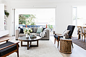 Gray upholstered sofa with cushions, round coffee table, armchair and side table in front of an open patio door in a bright living room