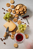 Cheese, grapes, nuts, cheese crackers cookies with glass of red wine and knife over white marble background