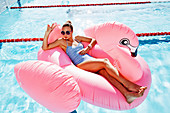 A young blonde woman wearing a blue bathing suit sitting on an inflatable swan