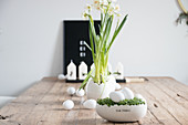 Easter arrangement of cress nest with white eggs, narcissus and candles on wooden table