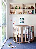 Baby cot and shelf in front of a floor-to-ceiling window in the children's room, toys on the carpet