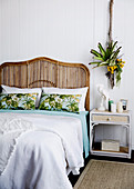 Rattanbett mit Betthaupt, Nachttisch und Pflanzendekoration im Schlafzimmer