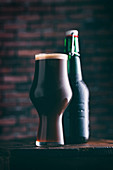 A glass of dark beer with a closed bottle of beer in the background