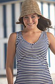Junge brünette Frau mit blauweiß gestreiftem Top und Sommerhut am Strand