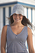 A young brunette woman on a beach wearing a blue-and-white striped top and a summer hat