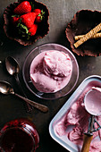 Strawberry ice cream in a cup and in a container with an ice cream scoop