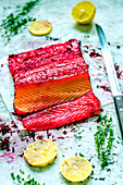 Gravlaks from salmon with beetroot, lemon wedges and fresh thyme lie on a concrete table