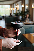 Hand holding a cocktail in a black stemmed glass