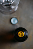 An opened beer bottle next to a bottle lid and a beer glass (seen from above)