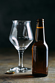 A bottle of beer with an empty beer glass and a bottle cap