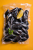 Cooked mussels sealed in plastic on a yellow surface