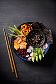 Sushi Buddha Bowl mit rotem Reis, Lachs, Nori, Gemüse und Sojasauce (Asien)