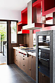 Küchenzeile mit Holzfronten und Einbaugeräten, darüber rotes Regal als Raumteiler