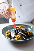 A chef drizzling cooked mussels with sauce