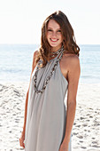 A young brunette woman on a beach wearing a beige summer dress and a necklace