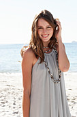 A young brunette woman on a beach wearing a beige summer dress and a necklace