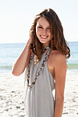 A young brunette woman on a beach wearing a beige summer dress and a necklace