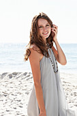 A young brunette woman on a beach wearing a beige summer dress and a necklace