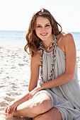 A young brunette woman on a beach wearing a beige summer dress and a necklace