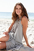 A young brunette woman on a beach wearing a beige summer dress and a necklace