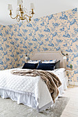 Double bed wiith headboard in romantic bedroom with floral wallpaper