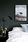 Double bed, side table, wall-mounted lamp and picture on dark wall in bedroom