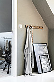 Row of coat pegs and pictures leaning against grey wall below sloping ceiling
