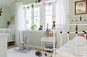 White metal bed, cot and green wallpaper in sibling's bedroom