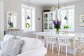 Weißer Esstisch mit Stühlen in offenem Wohnraum mit mit blau-weißer Tapete