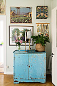 Blue, shabby-chic cabinet below various pictures on wall