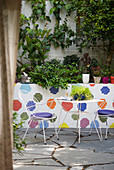 Filigraner Metalltisch und zwei Stühle auf Terrasse mit bunten Mosaik-Wandfliesen